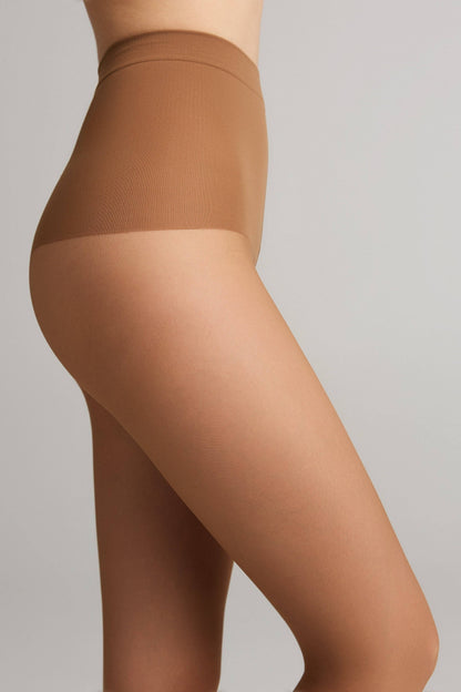 A person wearing tan-colored hosiery featuring a high-waisted shaping panel that extends to the upper thigh.