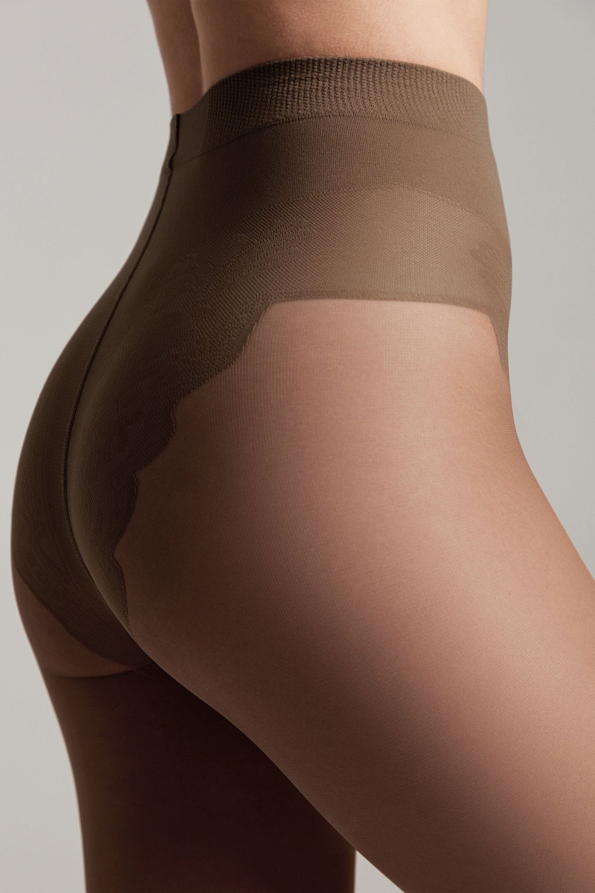A close-up view of the rear and side profile of a person wearing sheer brown tights with a reinforced opaque high-waisted control top section.