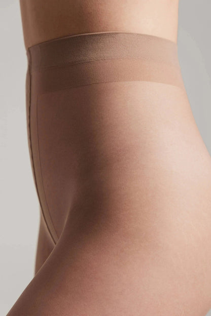 A close-up view of the upper part of beige pantyhose worn on a person's torso, featuring a wide elastic waistband and reinforced construction along the hip.