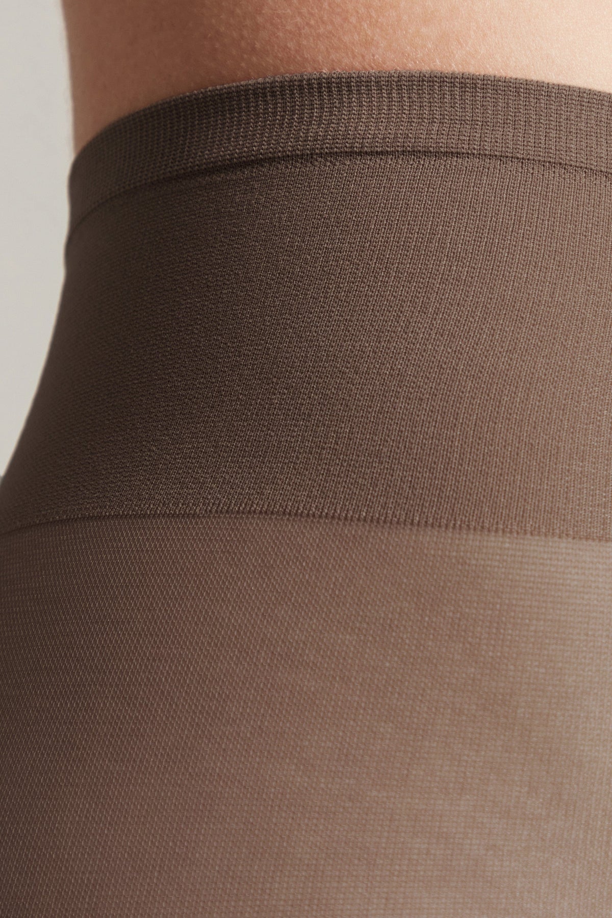 Close-up of brown tights featuring a wide, elasticated waistband against a person's skin.