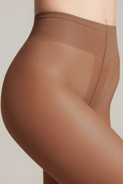 A close-up of light brown, sheer tights worn by a person, featuring a high-waisted design with reinforced seams along the hips and torso.
