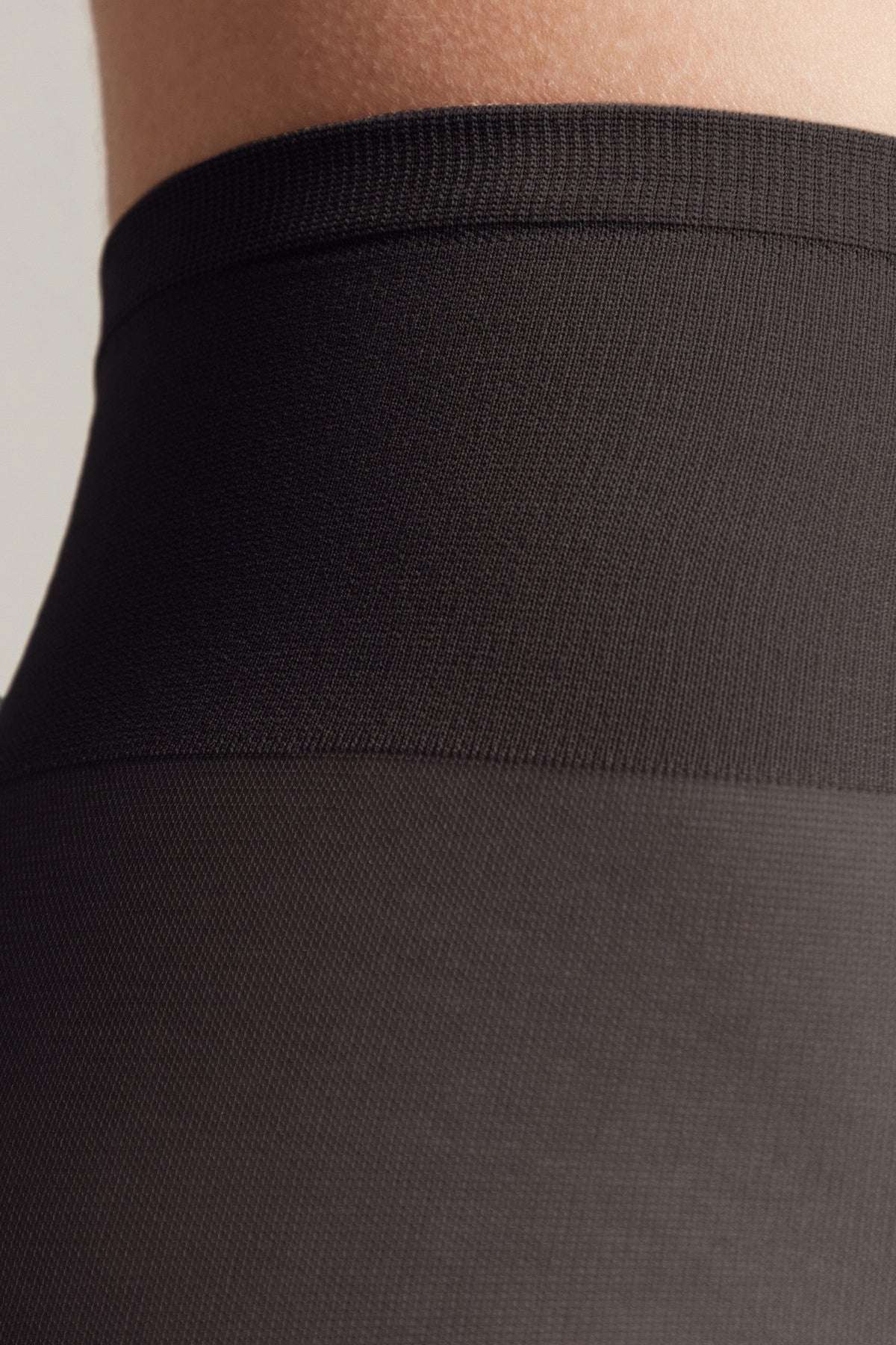 A close-up view of the black elastic waistband of a garment, showing the transition between the ribbed top band and the smoother opaque fabric below.