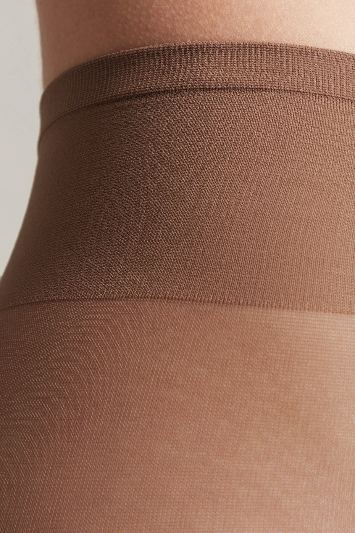 Close-up view of the waistband and upper leg portion of brown opaque tights.