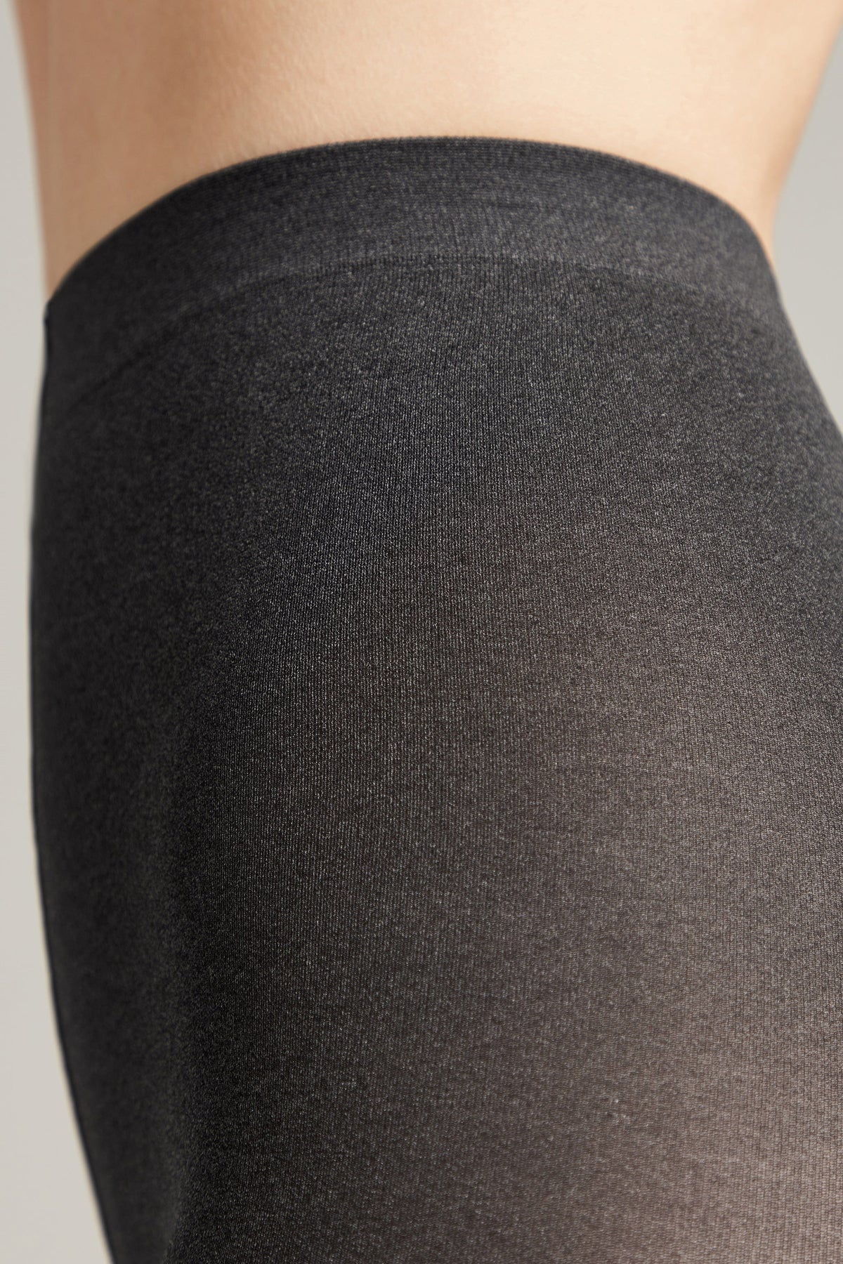 A close-up of charcoal grey tights worn against skin, showing the textured fabric and the elasticized waistband.