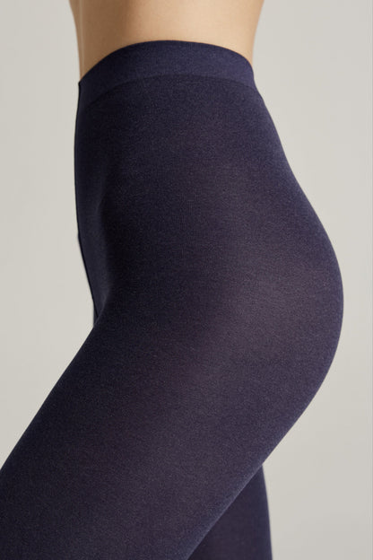 A close-up side view of a person wearing high-waisted, solid dark navy blue opaque leggings against a plain light grey background.