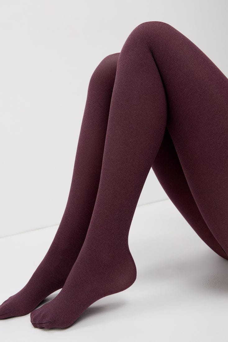A pair of opaque burgundy tights worn on a person's legs against a plain white background.