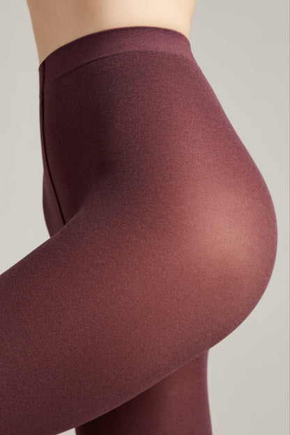 A close-up view of a person wearing maroon, opaque high-waisted leggings against a plain light grey background.