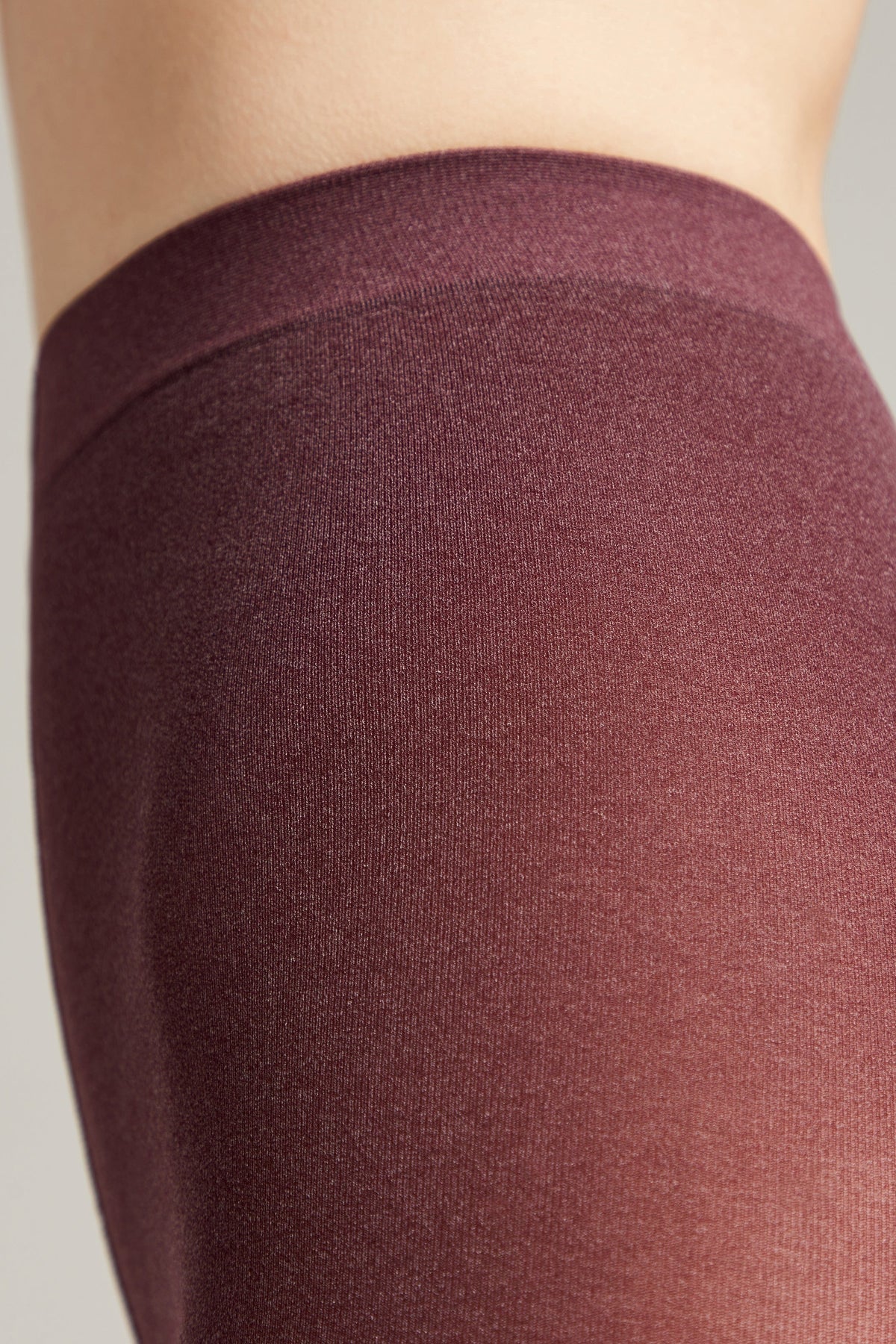 A close-up view of maroon opaque tights worn on a person, showing the fine knit texture and the elasticated waistband resting against the skin.