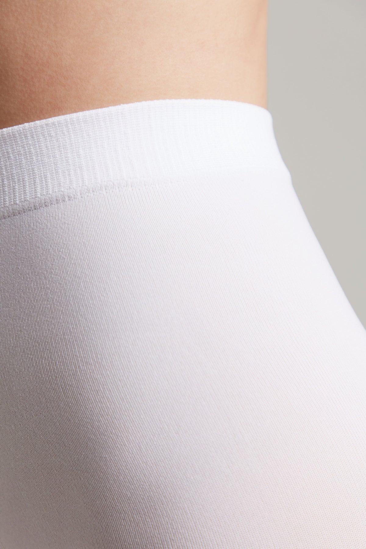 A close-up view of white, fitted fabric with a ribbed waistband worn on a person's torso against a plain background.