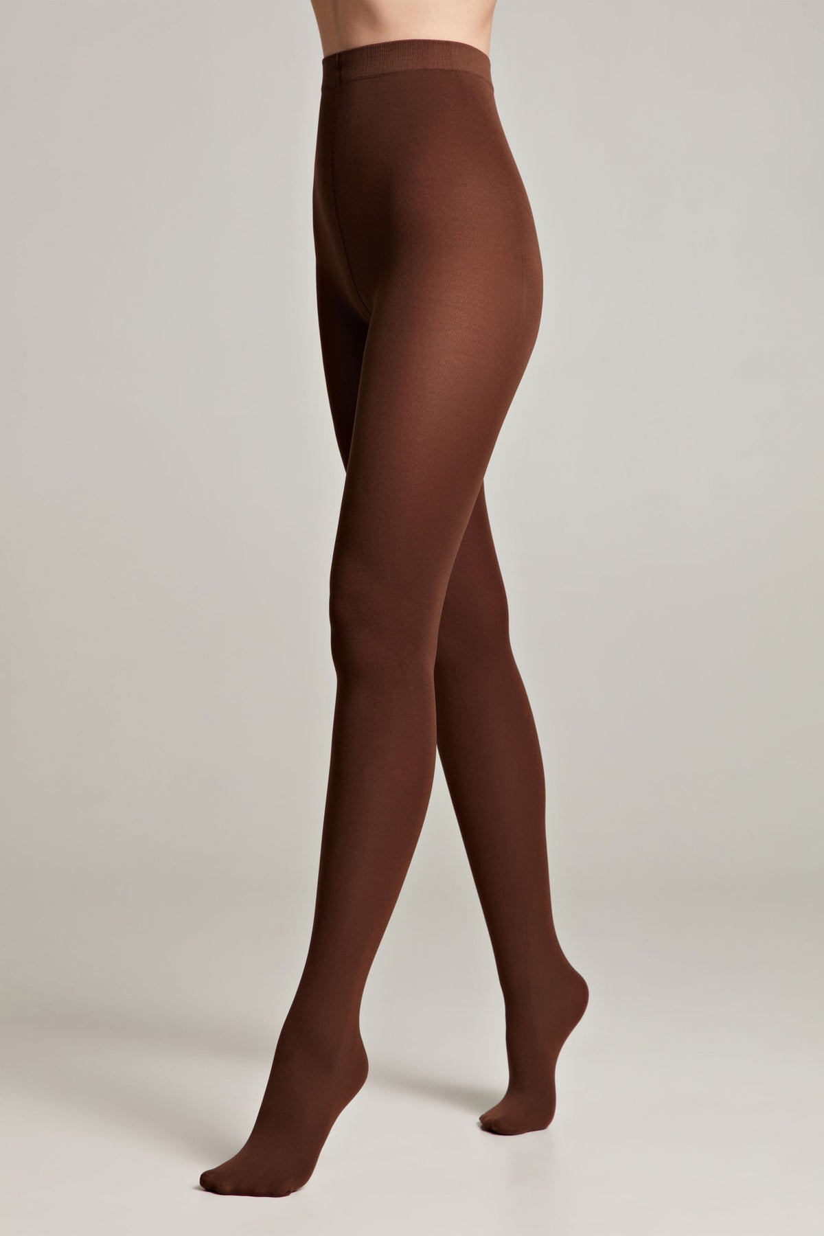 Opaque chocolate brown tights are worn on a person standing against a plain light gray background.