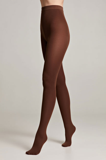Opaque chocolate brown tights are worn on a person standing against a plain light gray background.