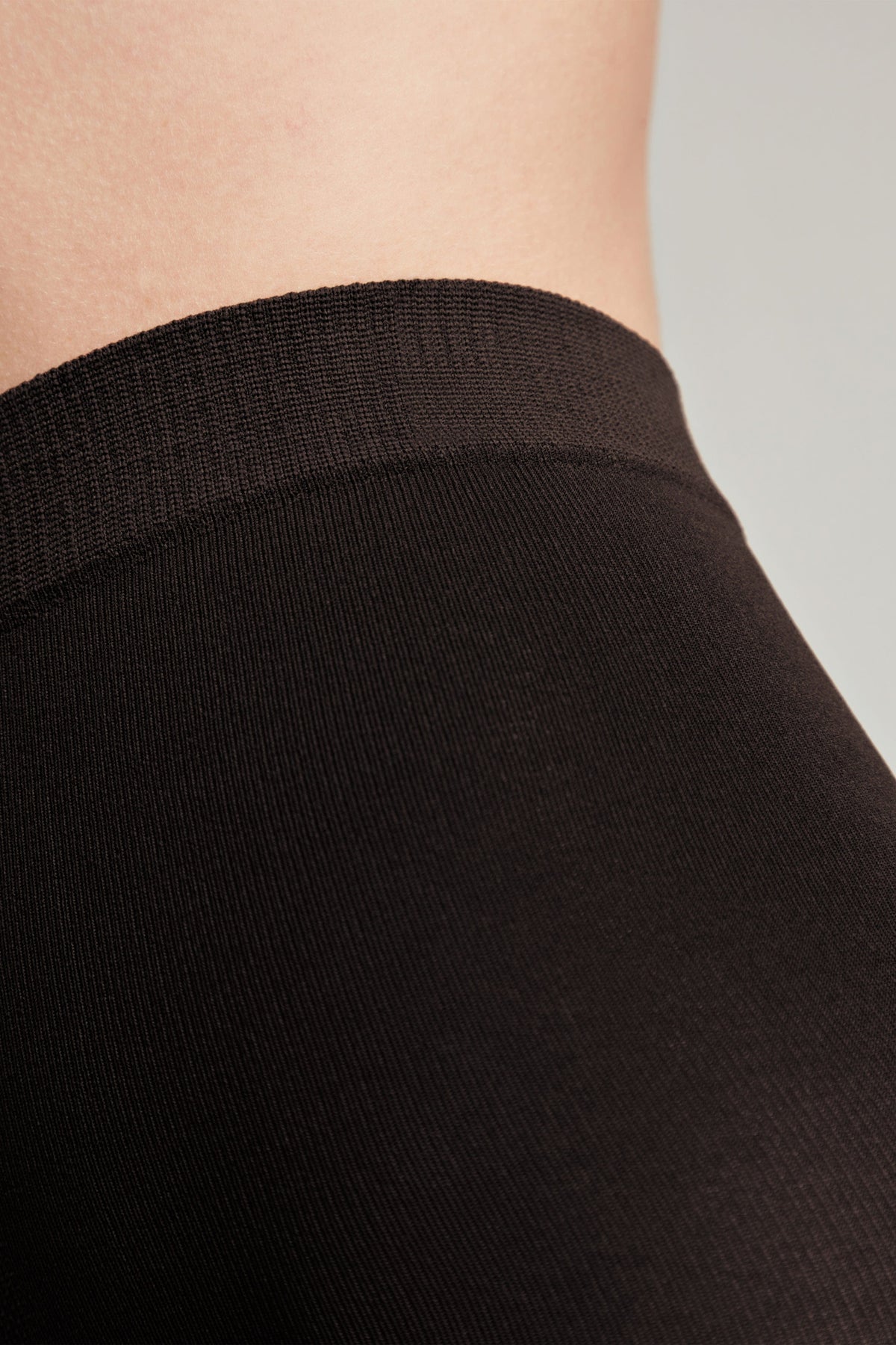 A close-up view of dark brown stockings worn on a person, showing the ribbed elastic waistband against skin.