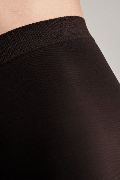 A close-up of brown leggings featuring a thick, ribbed elastic waistband worn against skin.