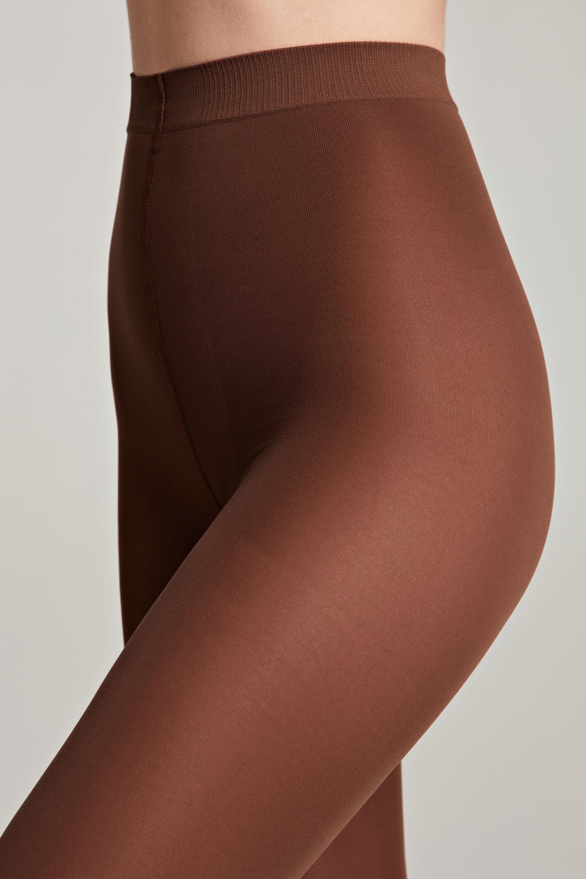 A close-up of a person wearing opaque, dark brown tights that extend from the upper thigh to the waist.
