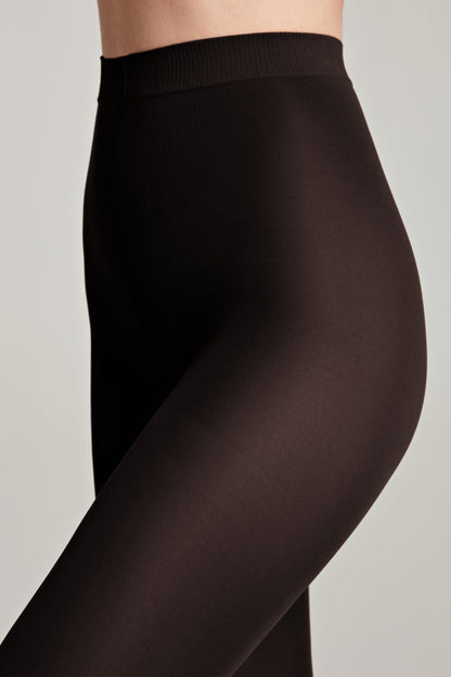 Black opaque tights worn on the lower torso and upper legs against a plain light gray background.