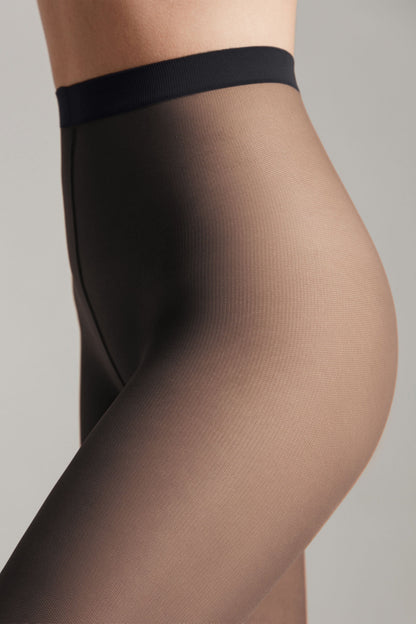 A close-up side profile view of sheer black tights featuring a thick, solid black waistband against a neutral gray background.