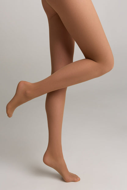 A pair of sheer tan tights worn on a person's legs against a plain grey background.