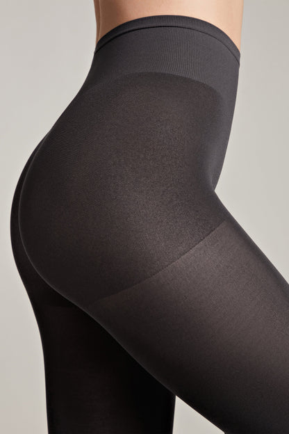 A close-up side view of a person wearing black opaque high-waisted tights against a plain light gray background.