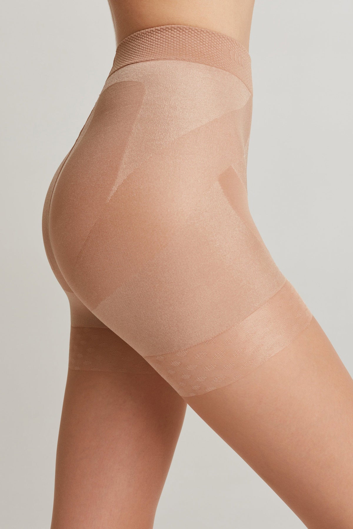 A close-up side view of nude-colored high-waisted shaping shorts with integrated compression panels on the hips and thighs.