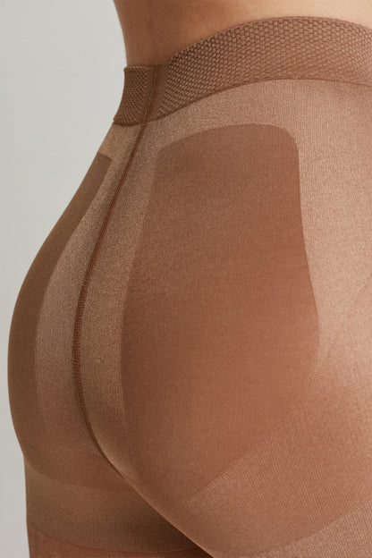 A close-up of nude-colored shapewear worn on a person, highlighting the textured fabric panels and reinforced seams around the hip and glute area.