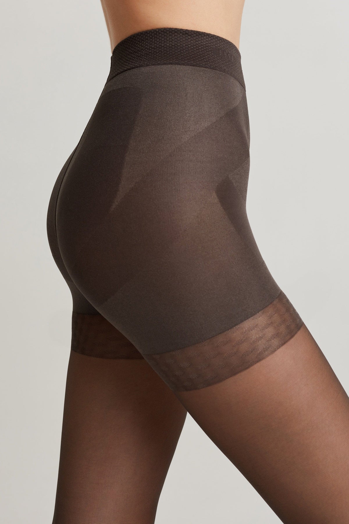 A side view of dark brown sheer shapewear shorts worn on a person, featuring a high-waisted textured waistband and a smooth, reinforced panel over the hips and thighs.