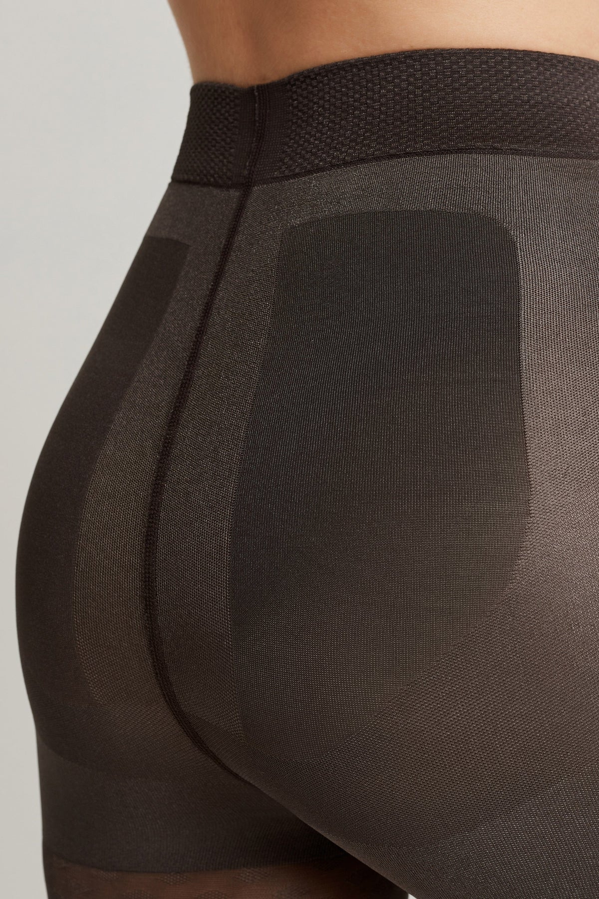 A close-up view of dark brown shaping tights featuring a high waistband and reinforced support panels on the hips and rear.