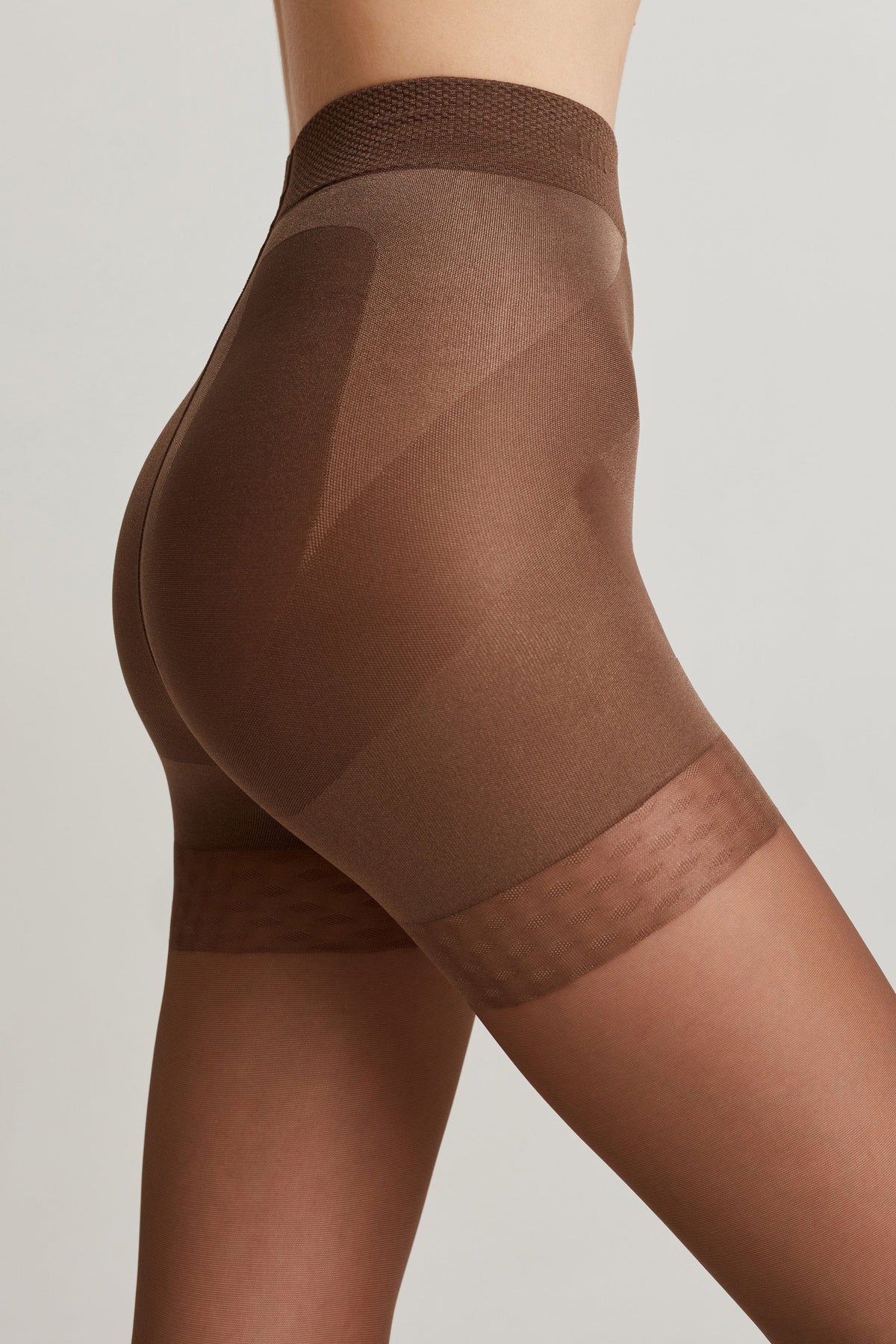 A close-up side view shows brown high-waisted shaping shorts with a reinforced texture panel on the hip and a wider, textured hem band against a light gray background.