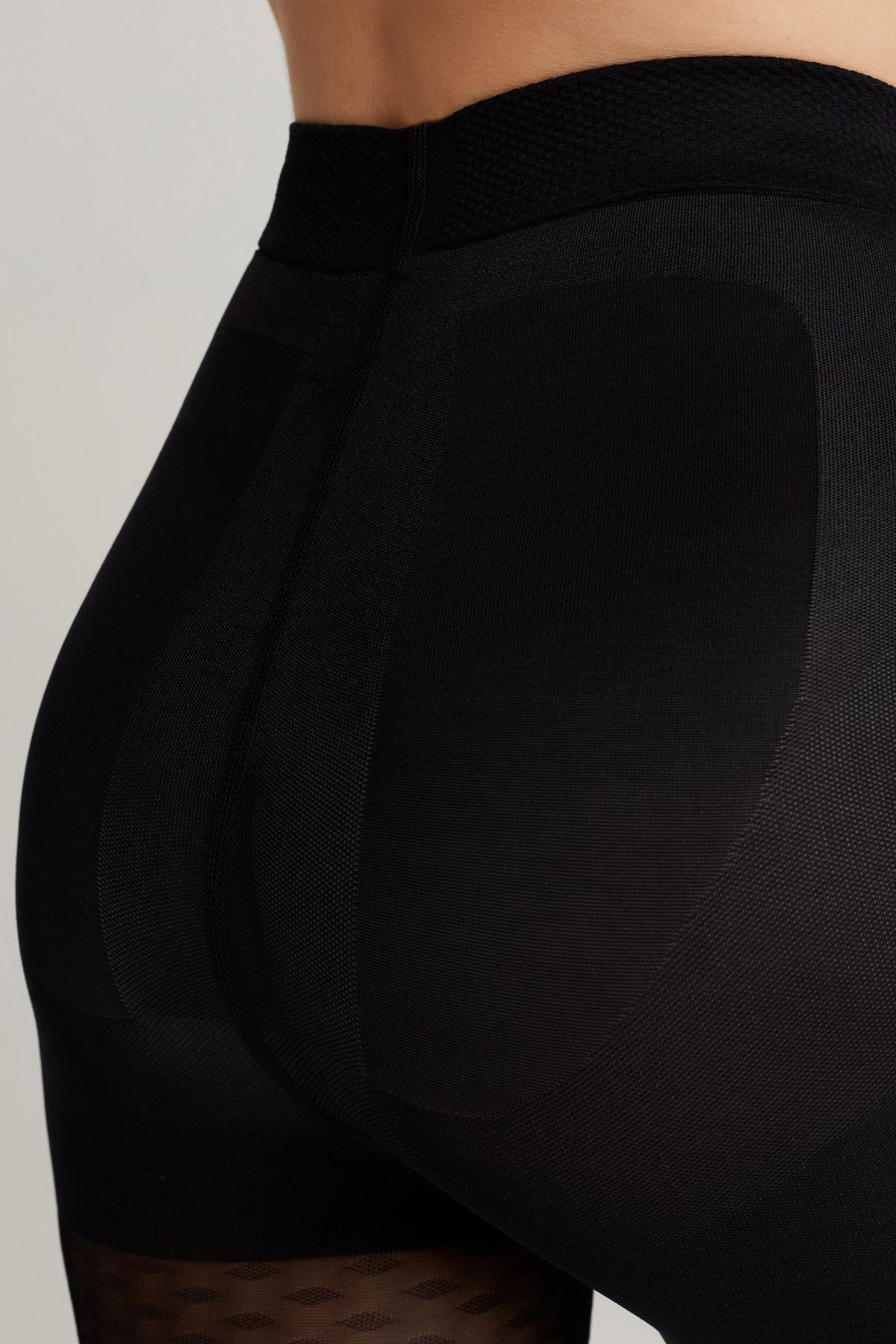 Black shaping tights feature a high waistband and reinforced panels designed for lift and compression.