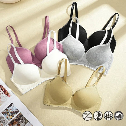 Three bras in white, black with grey, and tan colors are arranged on a beige surface, each featuring ribbed fabric, adjustable straps with text, and an underbust band.