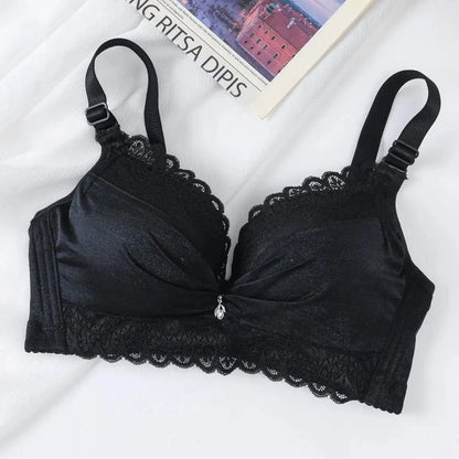 A black lace-trimmed brassiere with adjustable straps and a small decorative pendant at the center gore lies flat on a white fabric surface next to a book.