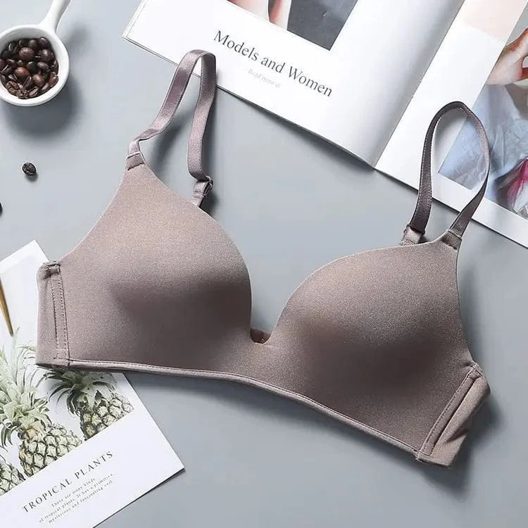 A beige wireless bra with smooth molded cups and adjustable straps, displayed on a grey surface next to a book and a bowl of coffee beans.