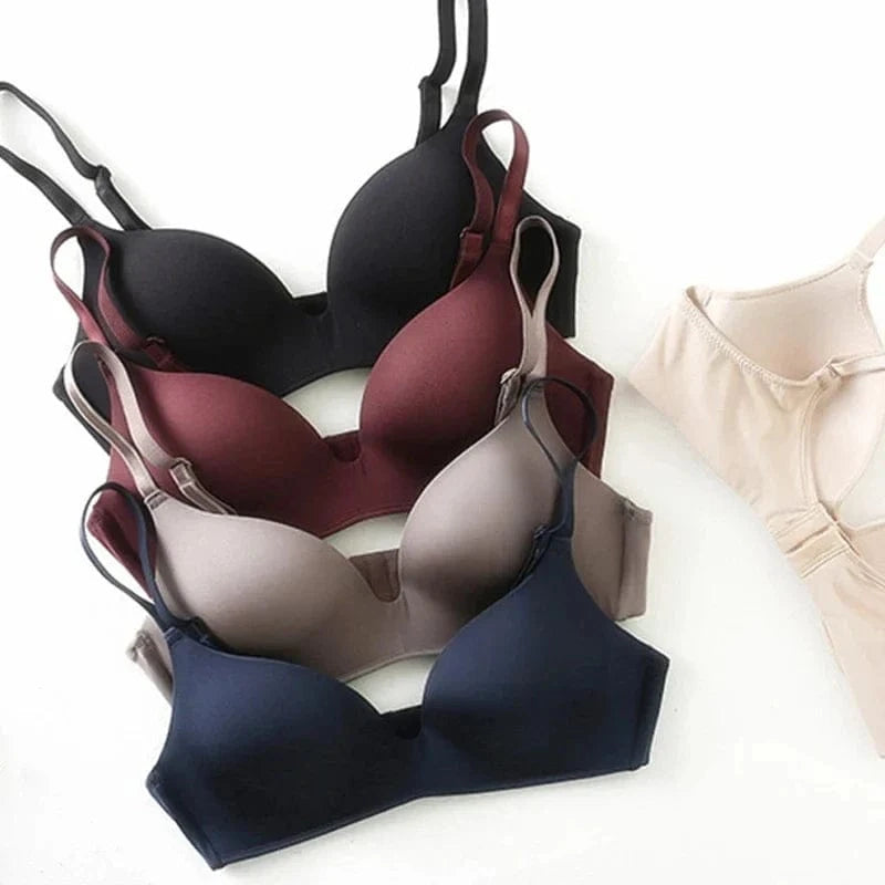 A set of five smooth, wireless bras in black, burgundy, taupe, navy blue, and beige arranged on a white surface.