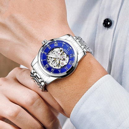 A silver-tone automatic watch with a blue circular dial, Roman numeral indices, and an exposed mechanical skeleton movement worn on a person's wrist.