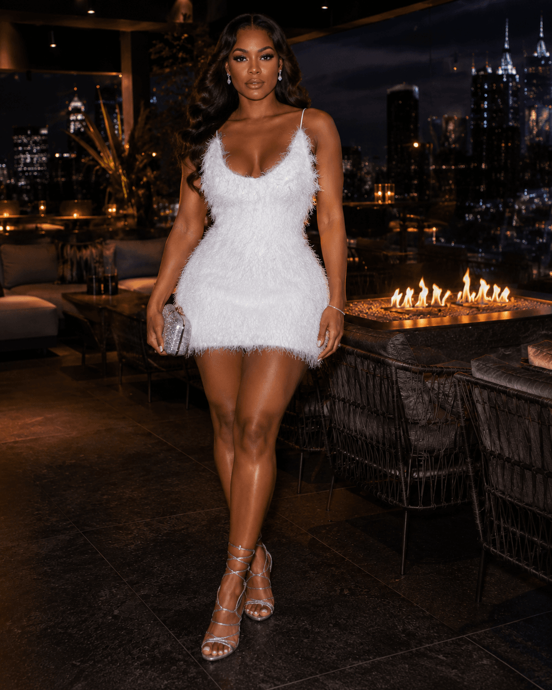 A white mini dress with a textured, fuzzy finish and thin spaghetti straps is worn by a woman standing on an outdoor patio at night.
