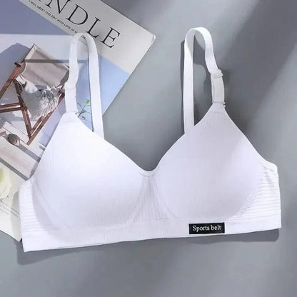 A white bralette with adjustable straps and a small black patch on the underbust band that reads Sports belt, displayed on a gray surface next to a magazine.