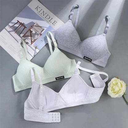 Three soft, wireless bras in grey, light green, and white are arranged on a grey surface next to a magazine and a white artificial flower.