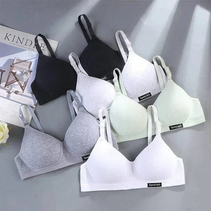Five seamless bralettes in black, light grey, dark grey, white, and mint green are arranged on a grey surface next to a fashion magazine.