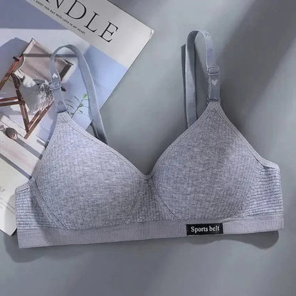 A grey ribbed bralette with adjustable straps and a small black label reading Sports belt on the bottom band, laid flat against a light grey surface next to a magazine.