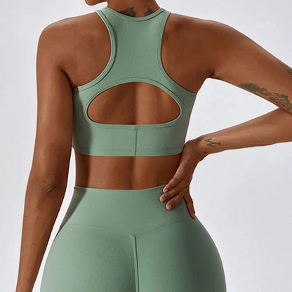 A sage green ribbed racerback sports bra with a large cutout detail on the back worn with matching high-waisted leggings.