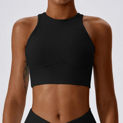 A black athletic crop top with a high neckline and a curved seam detail across the chest worn by a woman with a toned midriff.