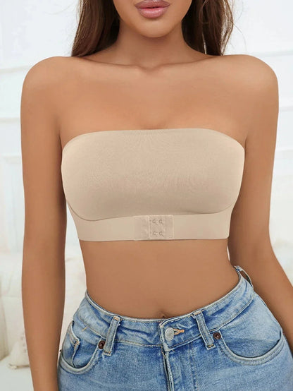 A beige strapless bandeau bra featuring a front hook-and-eye closure worn by a woman with blue denim jeans.