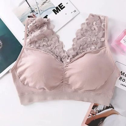A beige v-neck bralette with wide lace straps lies flat on a white surface next to pieces of paper and a small pink bottle.