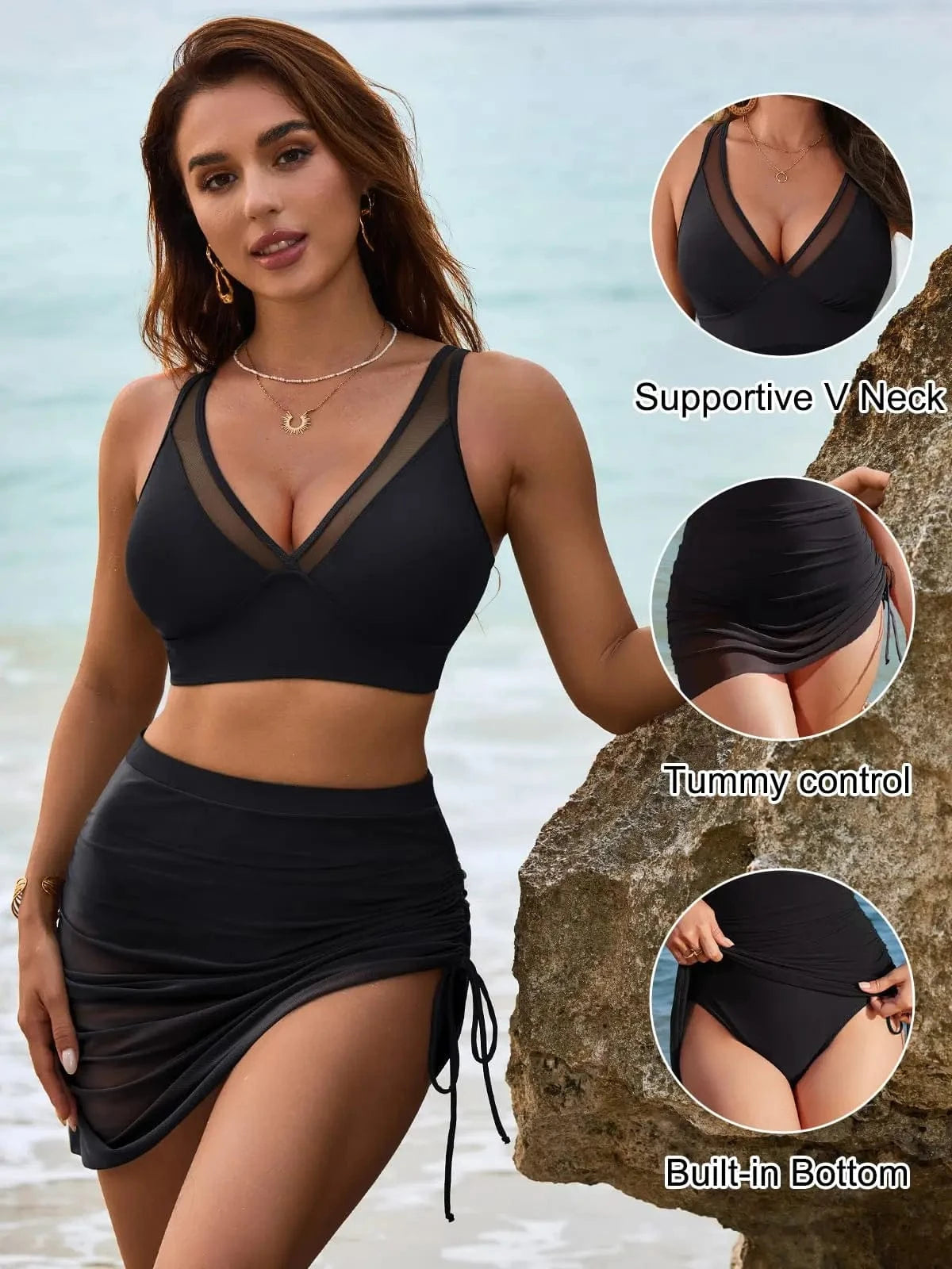 A woman stands on a beach wearing a black two-piece swimsuit with a V-neck top and a skirted bottom featuring side ruching and an internal brief.