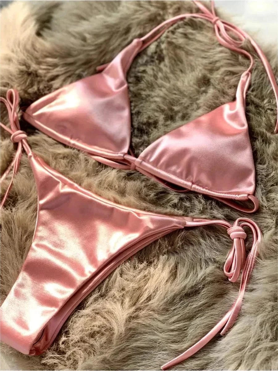 A metallic pink satin string bikini set displayed on a textured brown faux fur background.