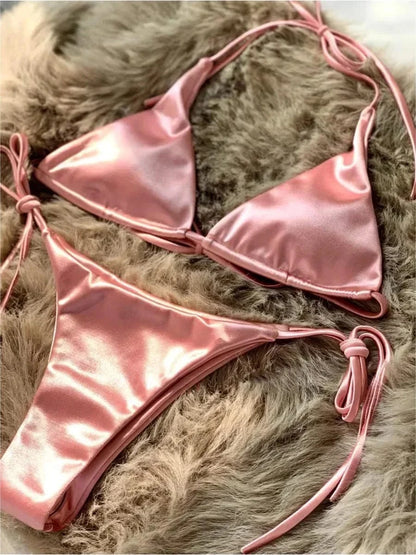 A metallic pink satin string bikini set displayed on a textured brown faux fur background.