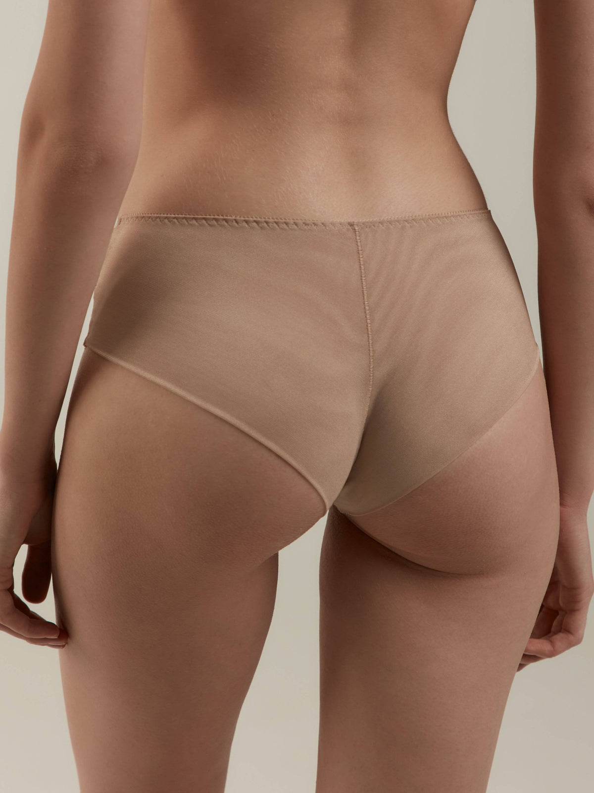 Nude-colored seamless briefs worn from the back against a plain light background.
