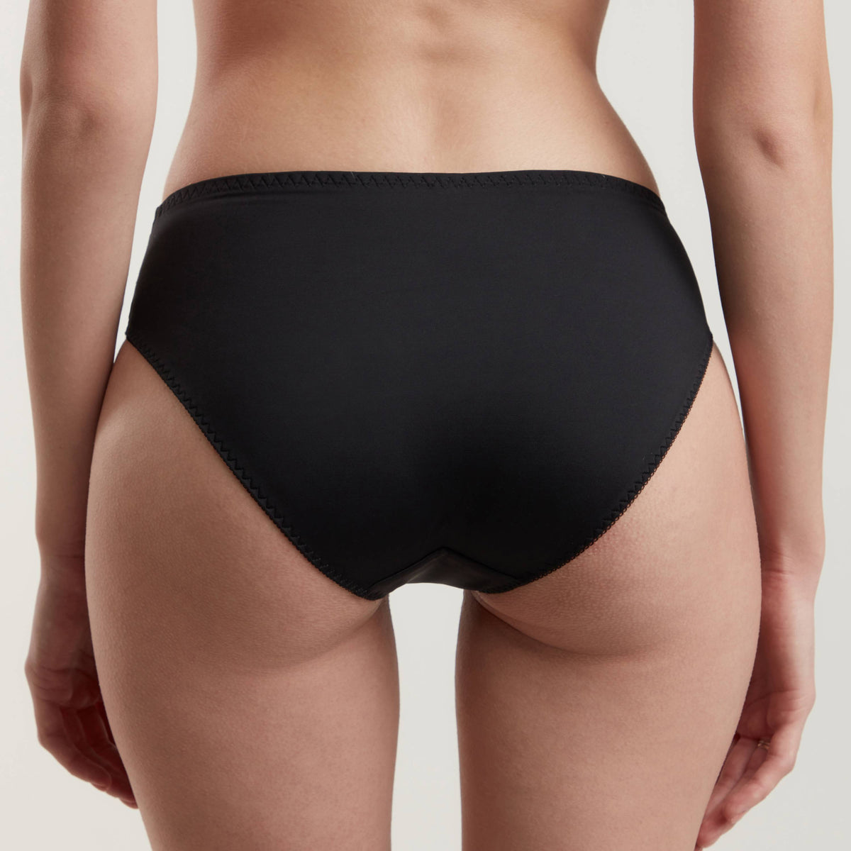 Black bikini-style panties with a simple cut worn from the back view against a plain light gray background.